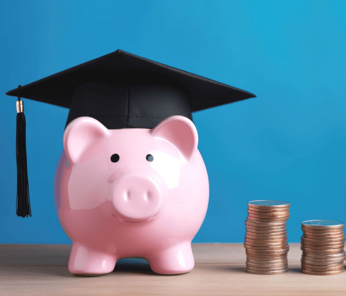 piggy bank wearing graduation cap next to stacks of coins