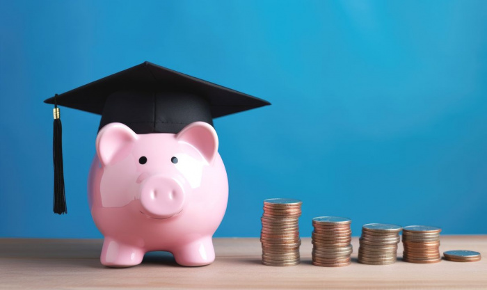 piggy bank wearing graduation cap next to stacks of coins