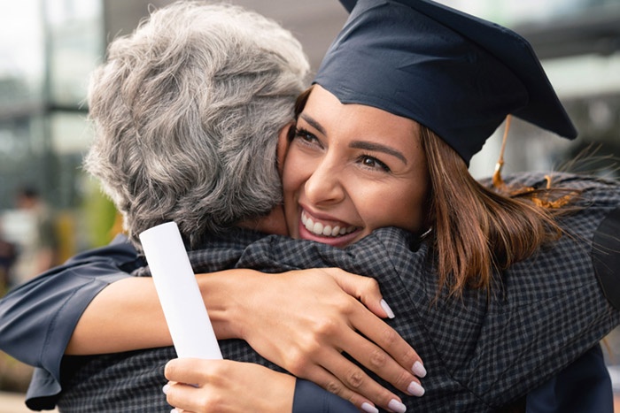 Student in cap and gown with diploma in hand hugging parent