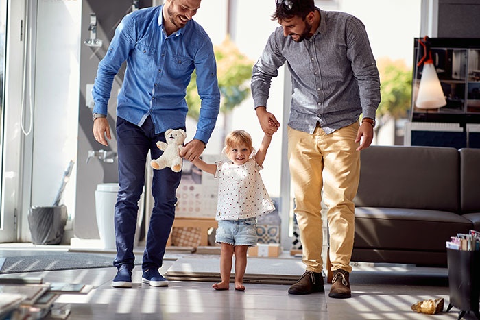 Two men helping toddler walk