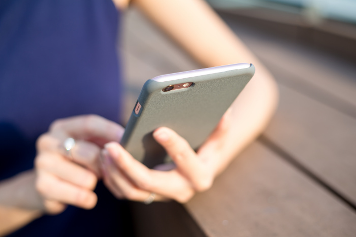Woman holding grey cell phone and typing with index finger