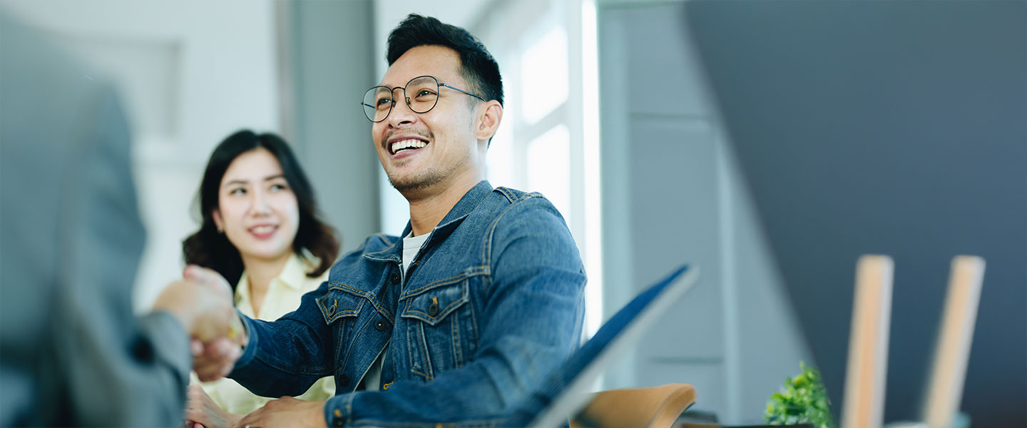 Young man shaking hands with out-of-frame assistant, smiling